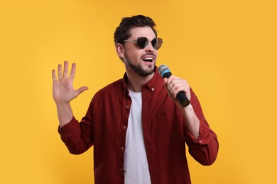 Handsome man with sunglasses and microphone singing on yellow background