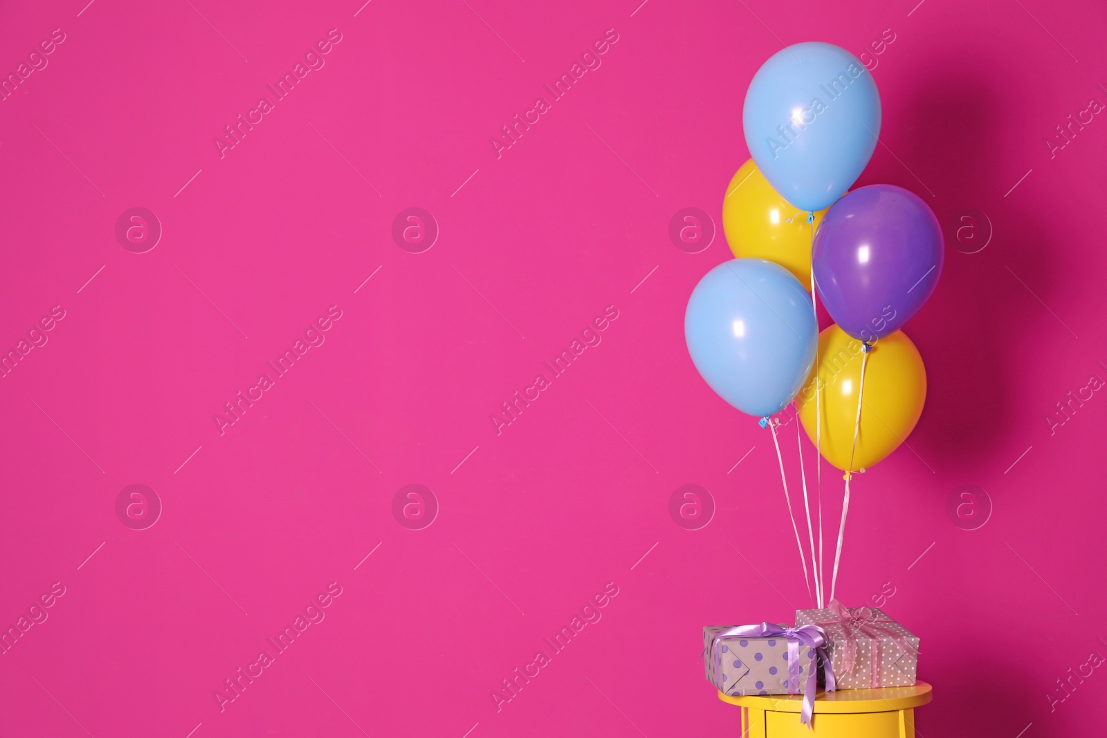 Photo of Bunch of bright balloons and gifts on table against color wall, space for text