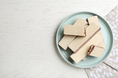 Photo of Plate of delicious crispy wafers with chocolate filling on white wooden table, top view. Space for text