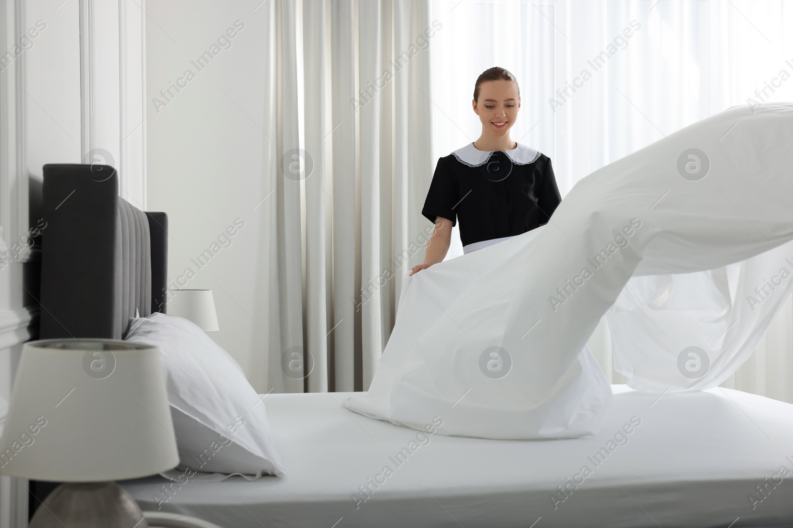 Photo of Young maid making bed in hotel room. Space for text