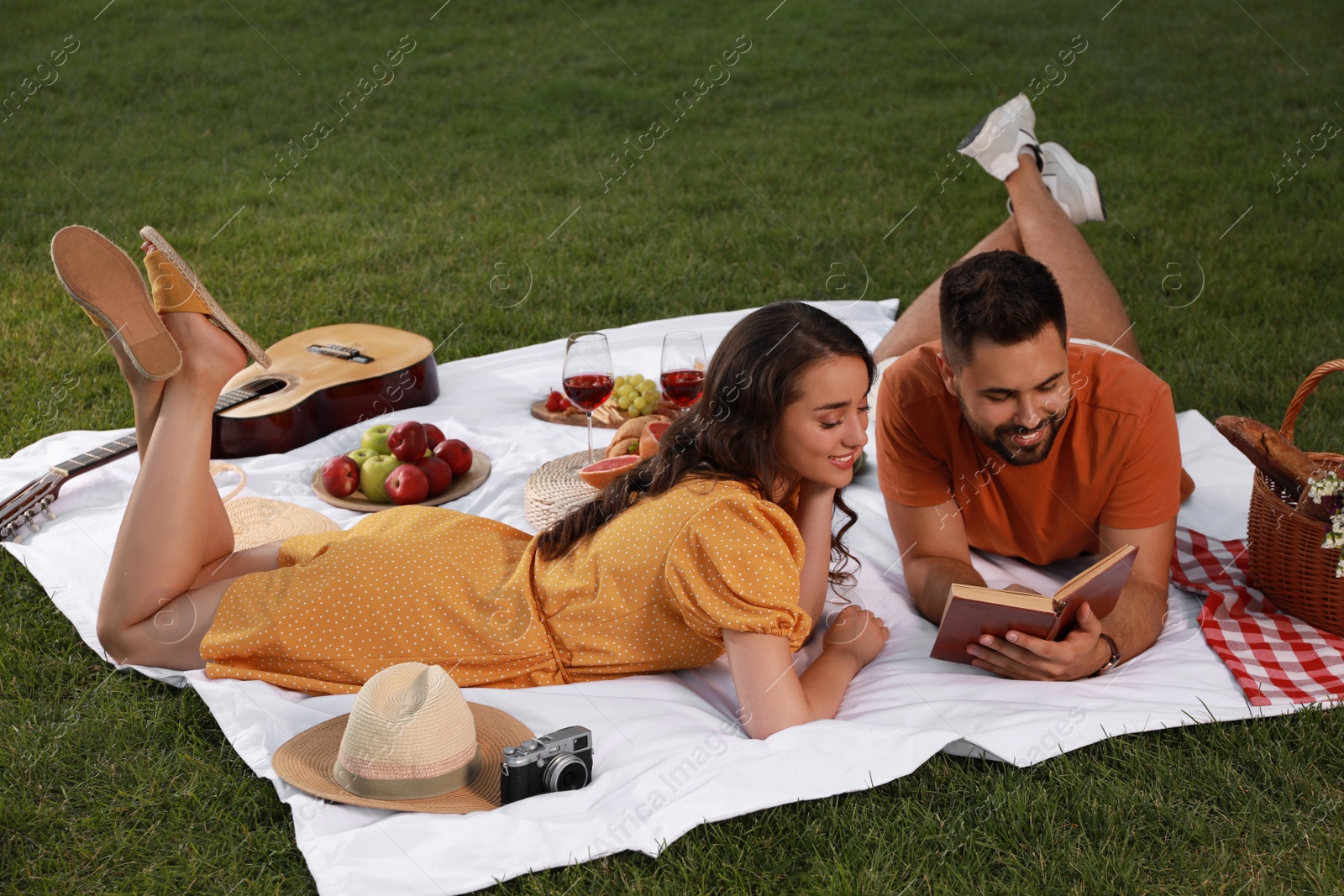 Photo of Happy young couple reading book on picnic plaid outdoors
