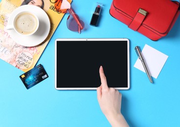 Online store. Woman using tablet on light blue background, top view