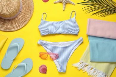 Beach towel, swimsuit, flip flops, hat and sunglasses on yellow background, flat lay