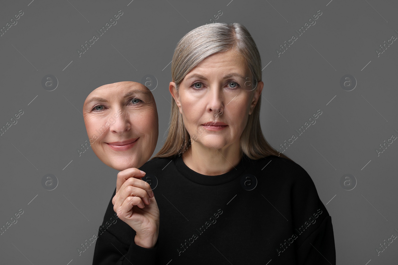 Image of Woman holding mask with her facial expression on grey background. Personality crisis, different emotions