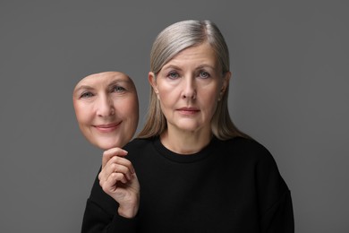 Woman holding mask with her facial expression on grey background. Personality crisis, different emotions