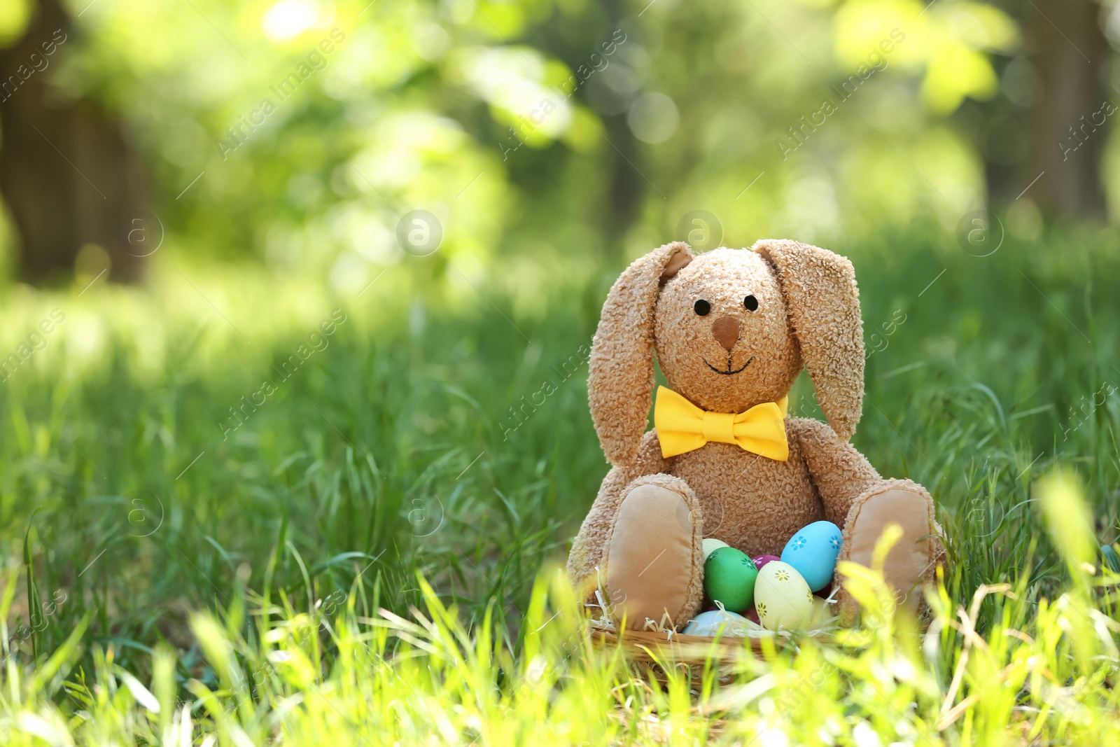 Photo of Toy bunny and basket with Easter eggs on grass