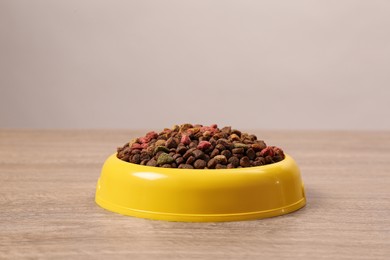 Photo of Dry food in yellow pet bowl on wooden surface