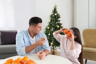 Photo of Happy couple with tangerines in room decorated for Christmas