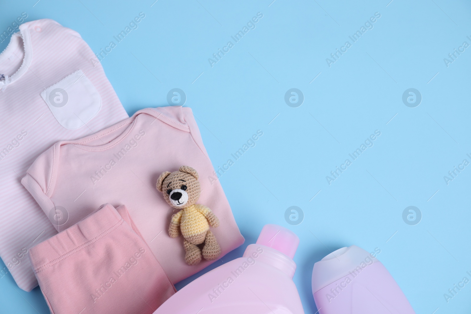 Photo of Bottles of laundry detergents, baby clothes and toy bear on light blue background, flat lay. Space for text