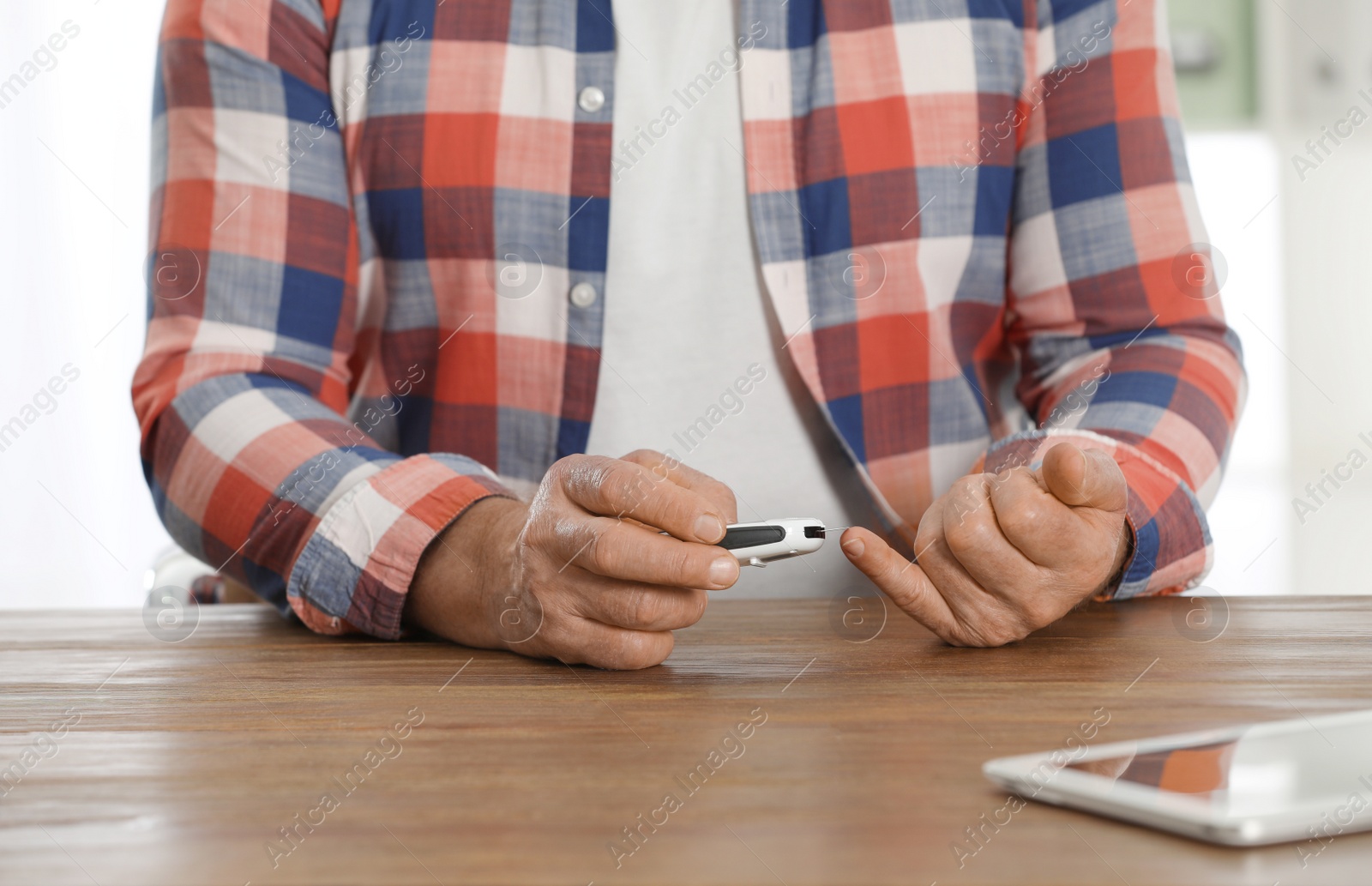 Photo of Senior man using digital glucometer at table, closeup. Diabetes control