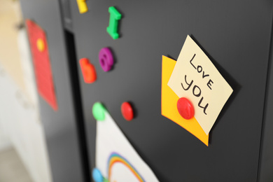 Note with phrase LOVE YOU and magnets on refrigerator, closeup