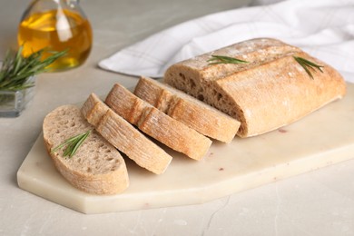 Photo of Cut delicious ciabatta with rosemary on white table