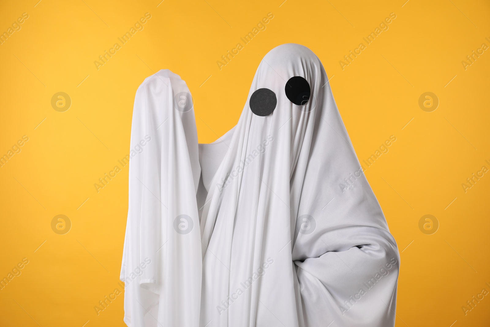 Photo of Creepy ghost. Person covered with white sheet on yellow background