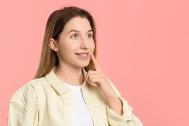 Photo of Portrait of smiling woman pointing at her dental braces on pink background. Space for text