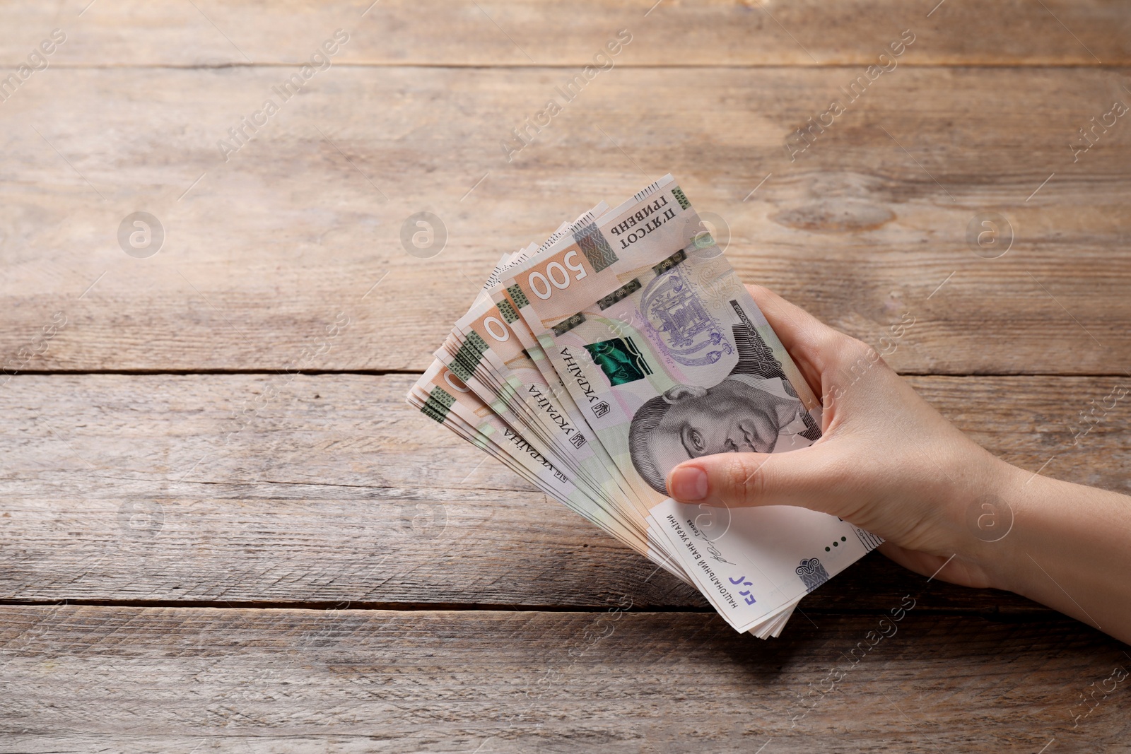 Photo of Woman holding Ukrainian money on wooden background, closeup