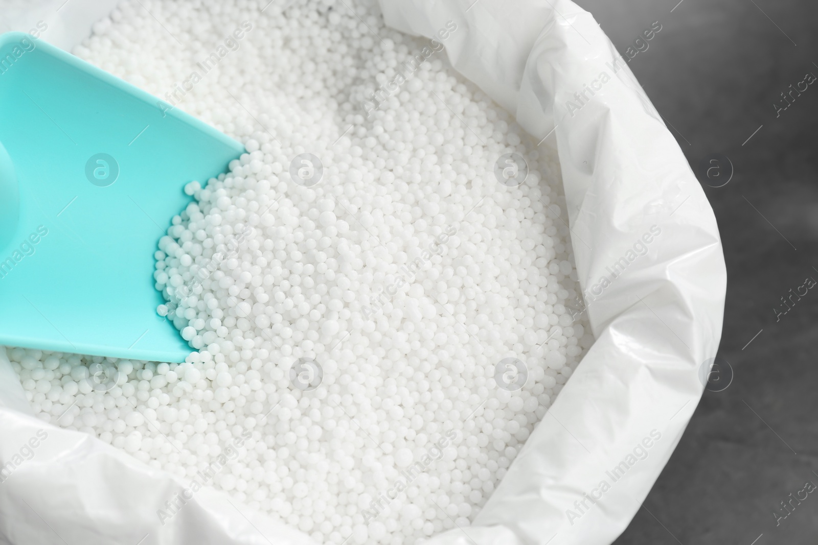 Photo of Bag with granular mineral fertilizer and scoop on grey background, closeup