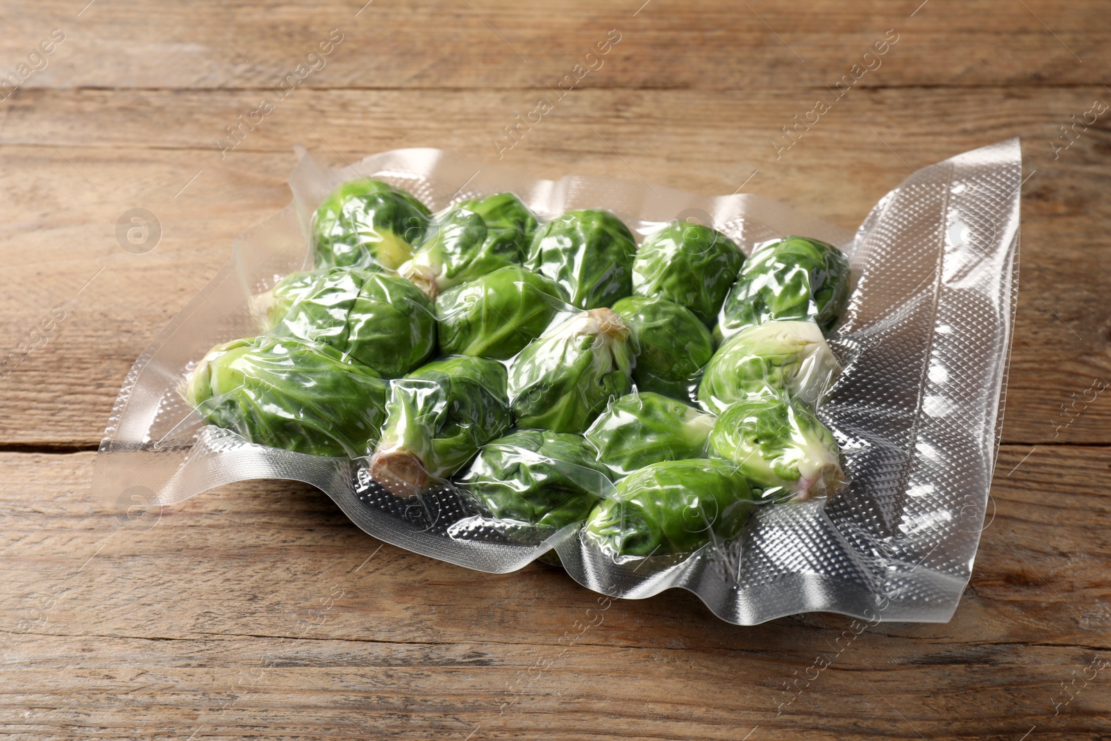 Photo of Vacuum pack of Brussels sprouts on wooden table