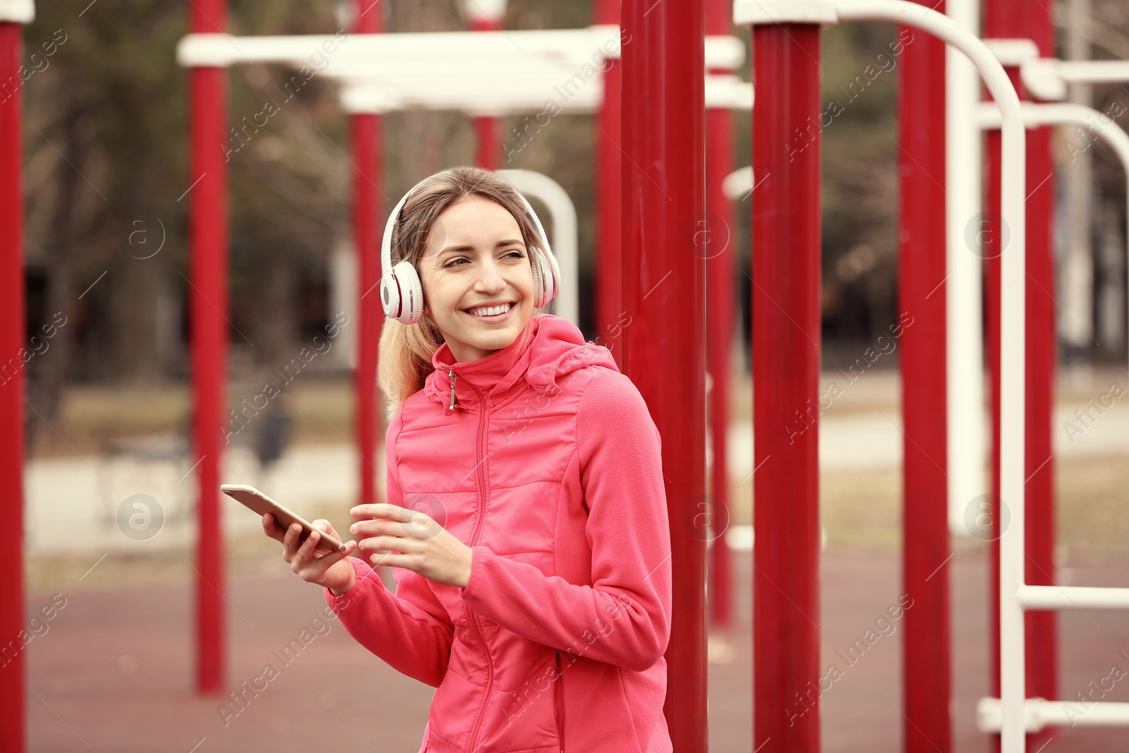 Photo of Young woman with headphones listening to music on sports ground