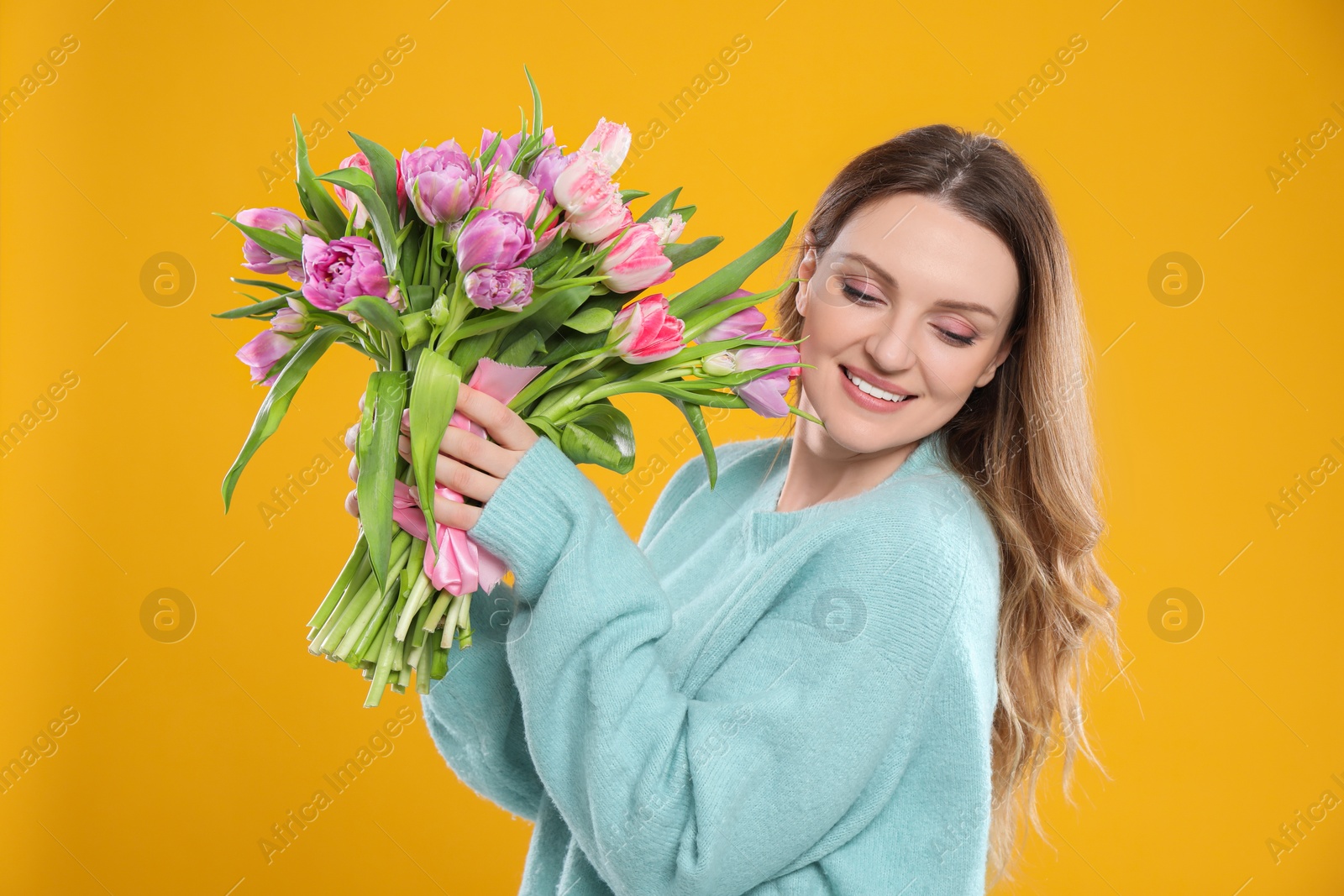 Photo of Happy young woman with bouquet of beautiful tulips on yellow background