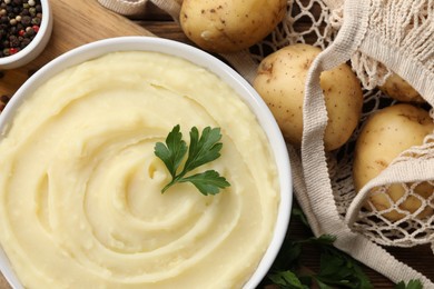 Bowl of tasty mashed potato, parsley and pepper on wooden table, flat lay