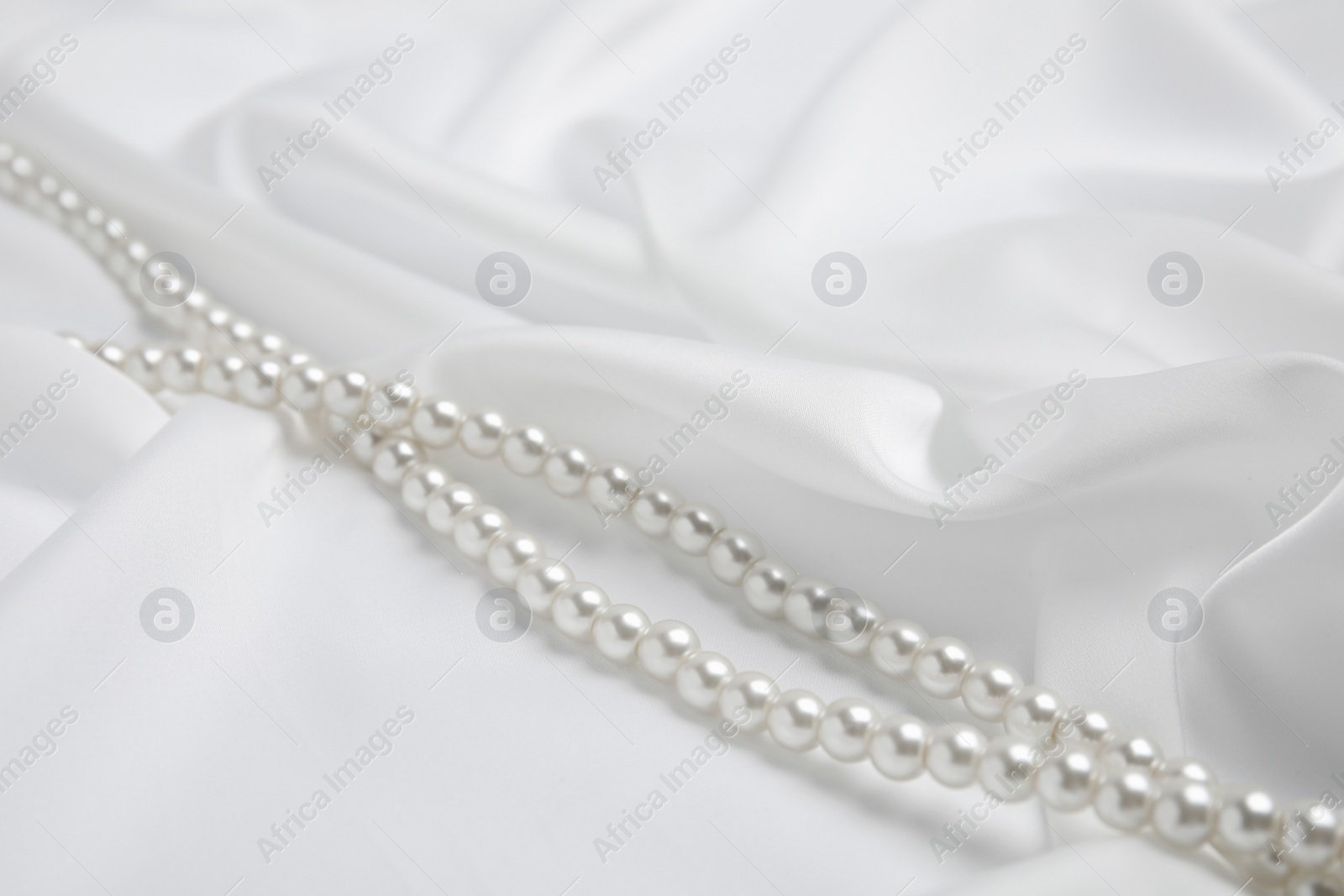 Photo of Beautiful pearls on delicate white silk, closeup