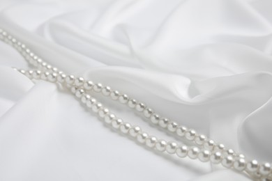 Photo of Beautiful pearls on delicate white silk, closeup