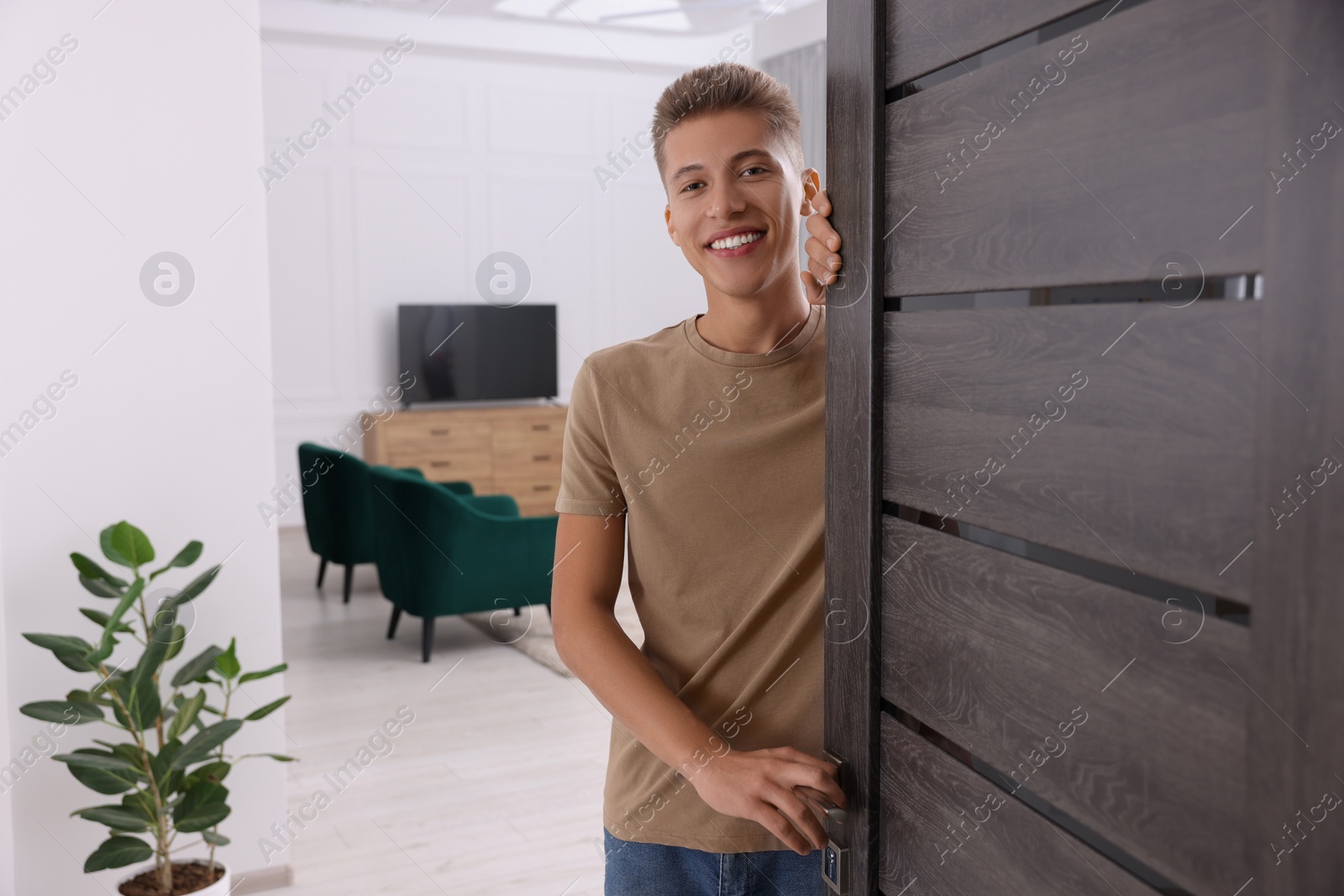 Photo of Happy man standing near door, space for text. Invitation to come indoors