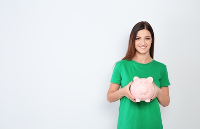 Young woman with piggy bank on white background. Space for text