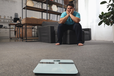 Photo of Scales and depressed overweight man on floor at home