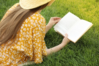 Photo of Young woman reading book on green grass, closeup
