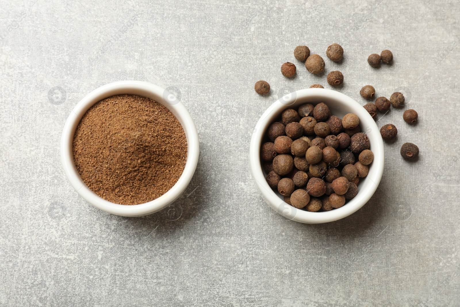 Photo of Ground allspice pepper and grains in bowls on grey table, top view