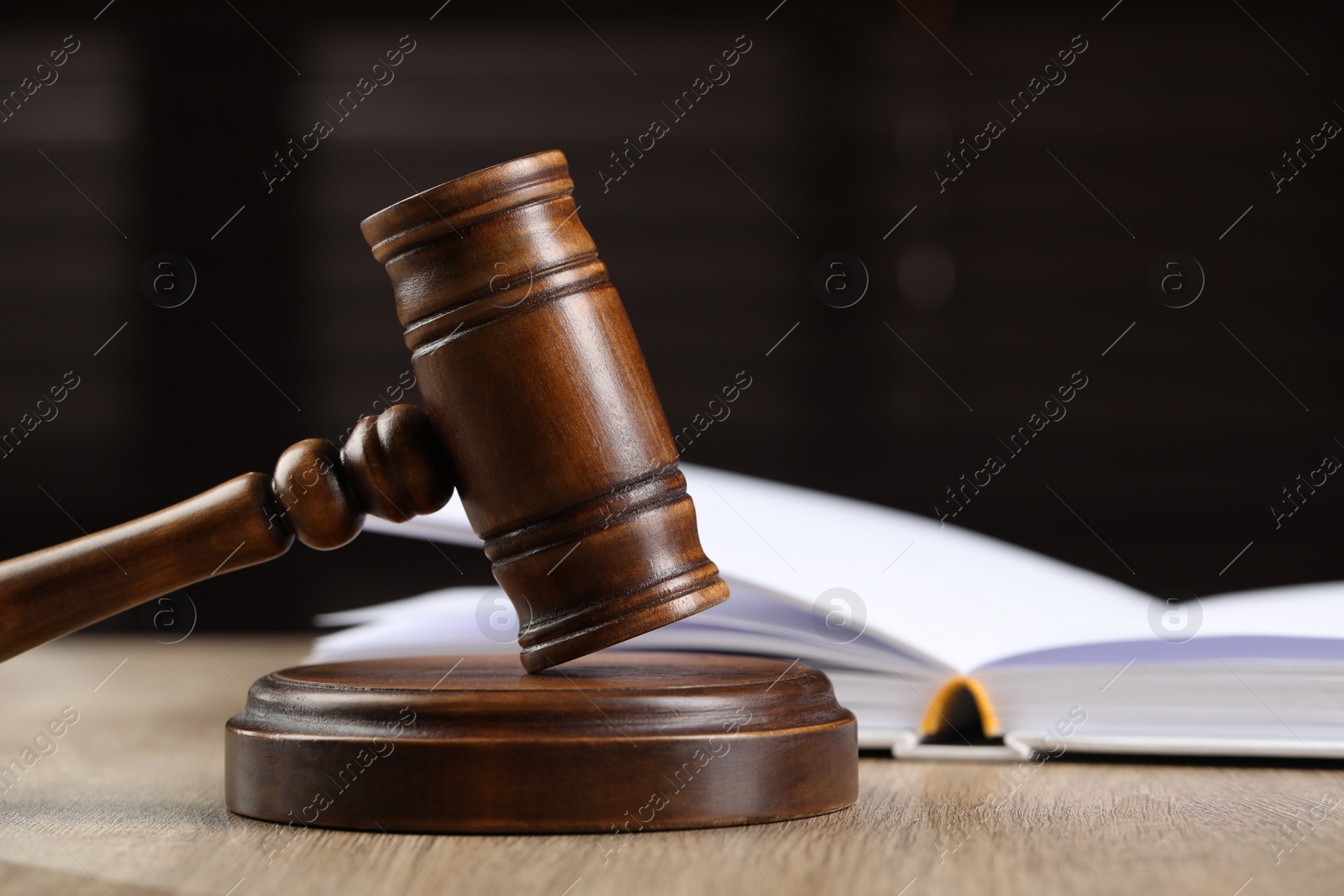 Photo of Wooden gavel and open book on table against dark background. Space for text