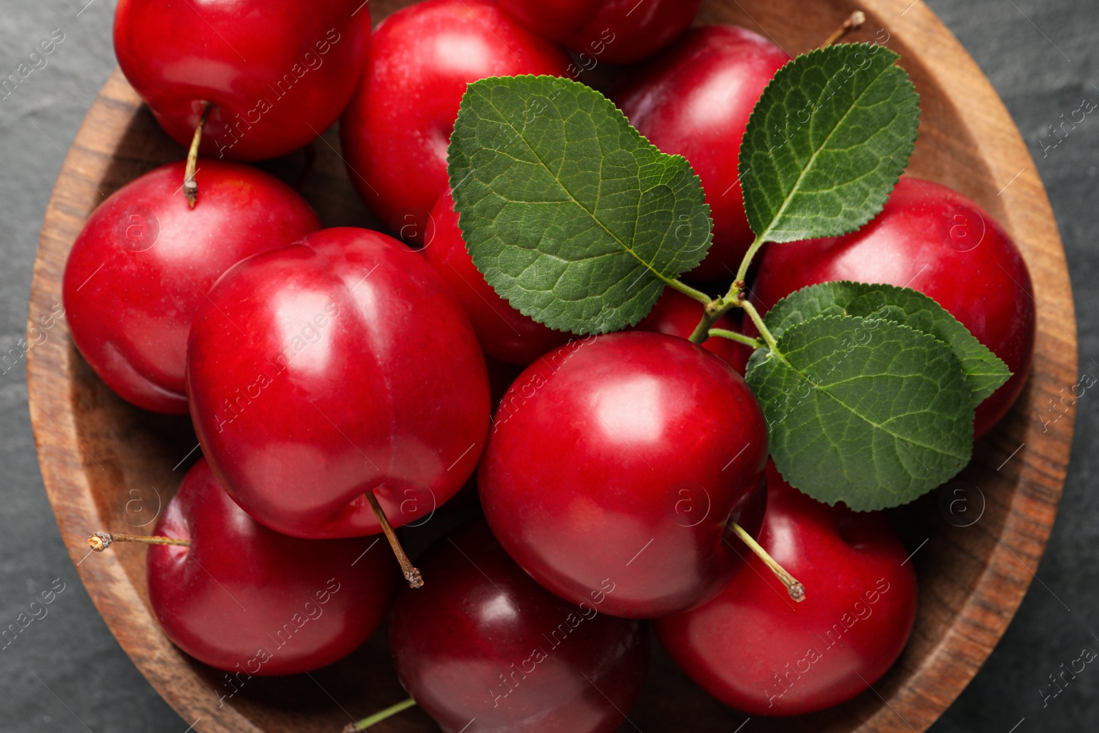 Photo of Delicious ripe cherry plums with leaves on black table, top view