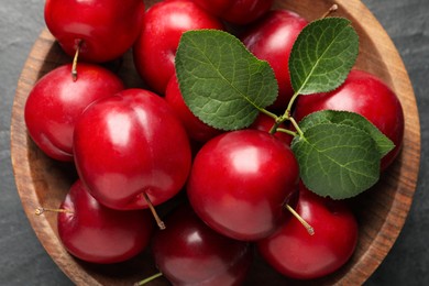 Delicious ripe cherry plums with leaves on black table, top view