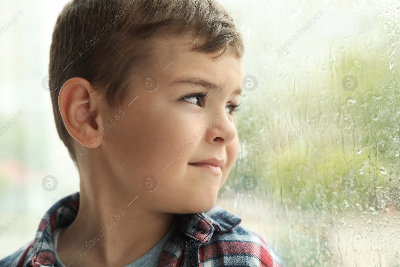 Photo of Cute little boy near window indoors, space for text. Rainy day