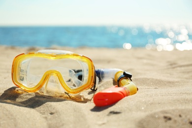 Diving mask and tube on sand near sea, space for text. Beach objects