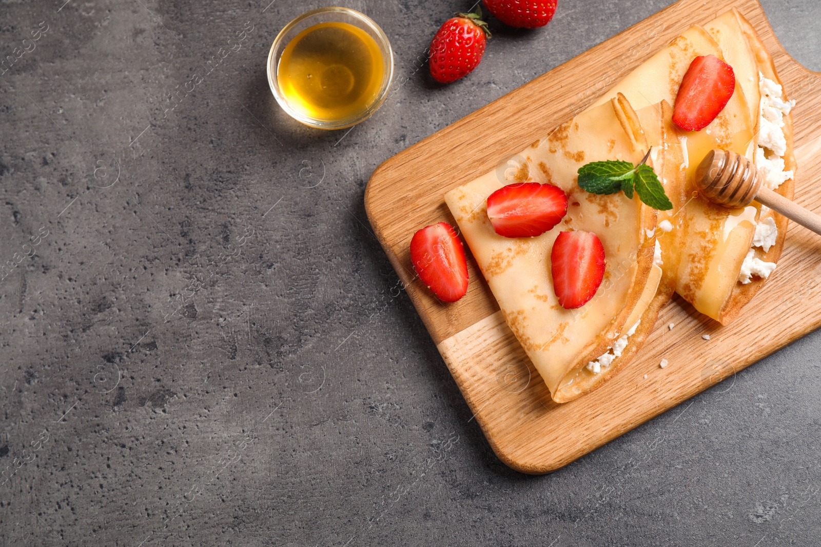 Photo of Delicious thin pancakes with strawberries, cottage cheese and honey on grey table, flat lay. Space for text