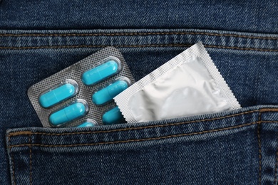 Photo of Jeans with pills and condom in pocket as background, top view. Potency problem concept