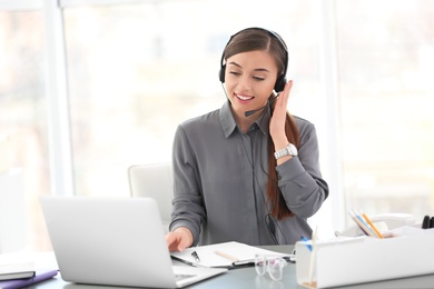 Photo of Young woman talking on phone through headset at workplace