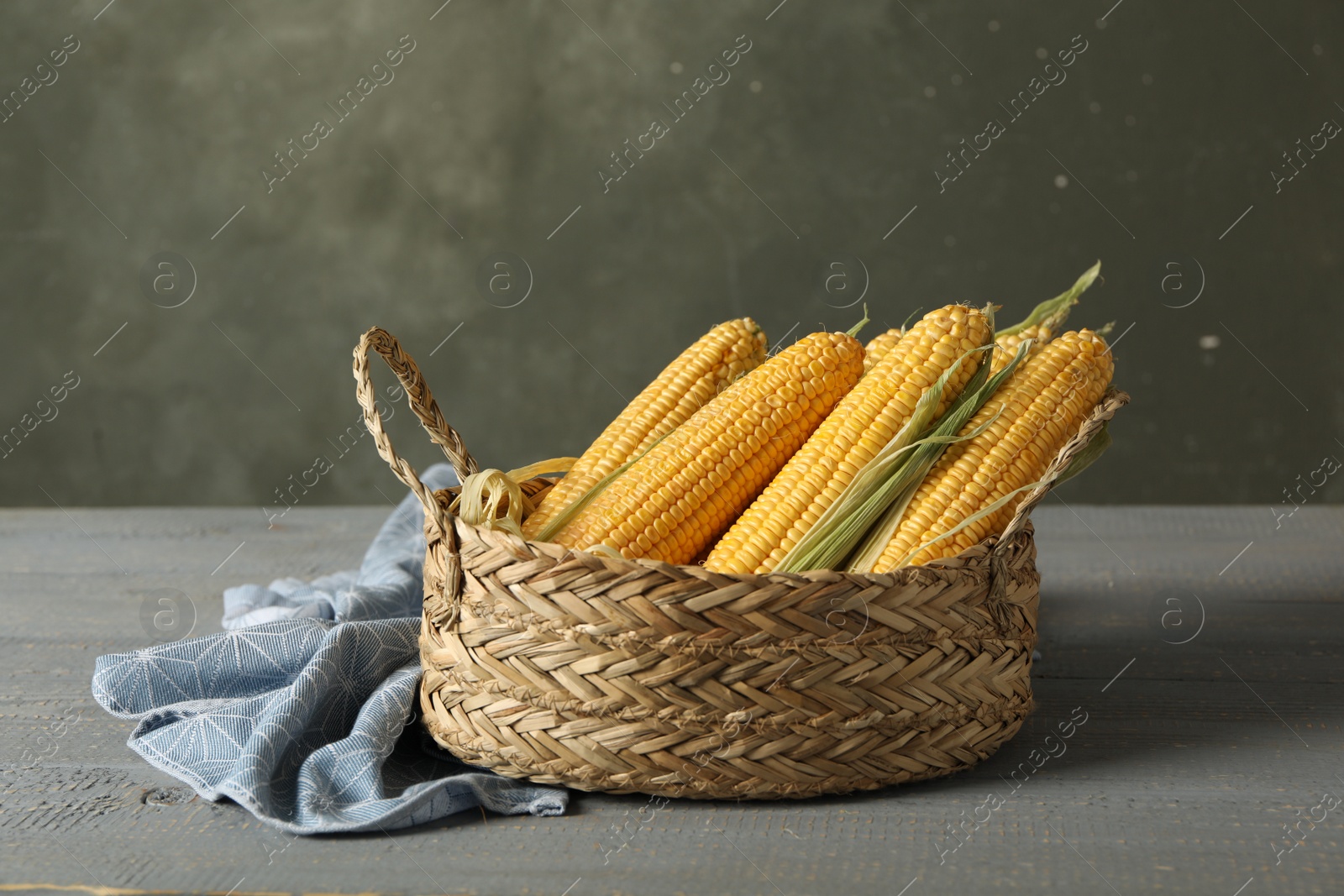 Photo of Basket of corn cobs on grey wooden table