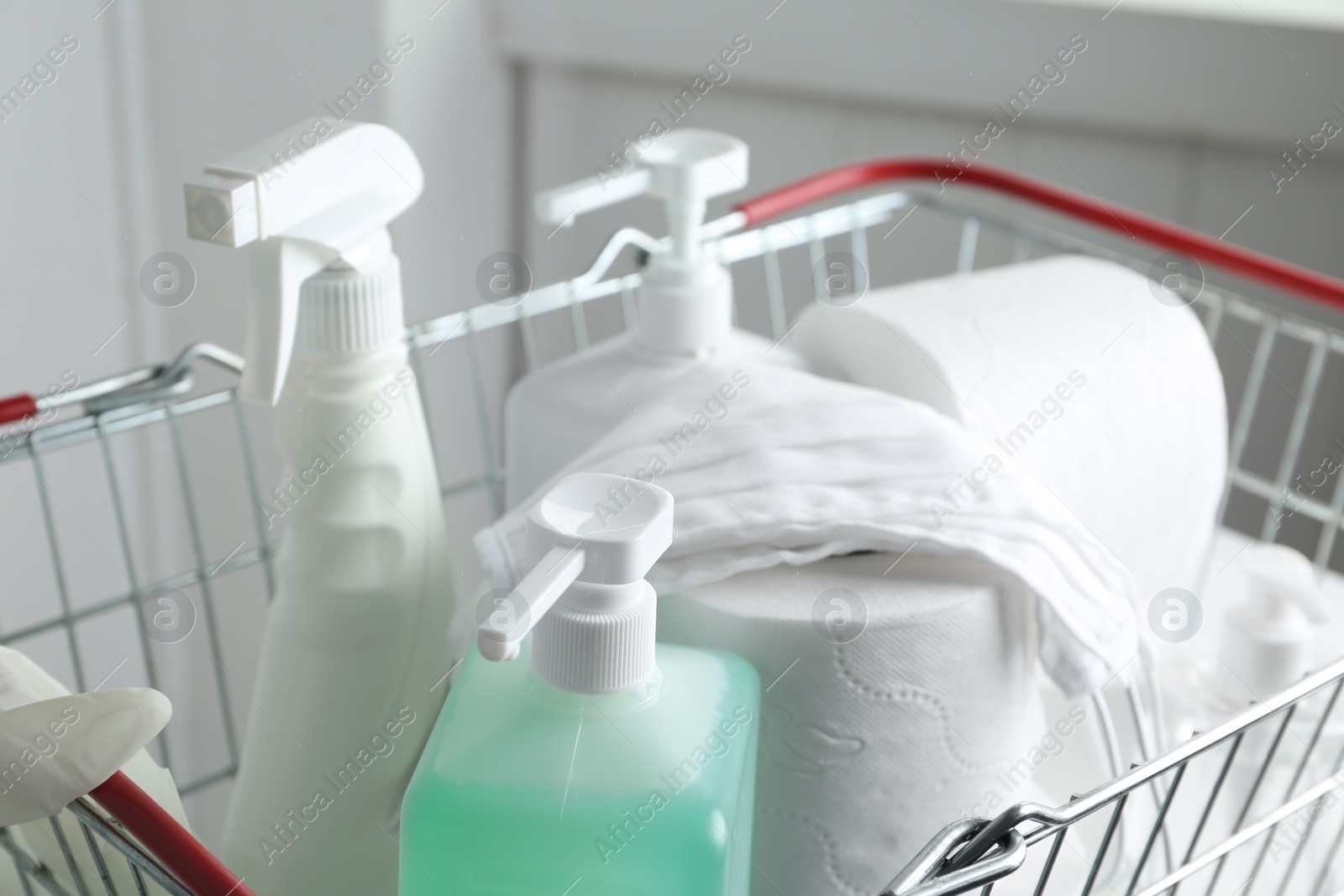 Photo of Shopping basket with antiseptics, toilet paper and masks on table indoors, closeup. Panic caused by virus