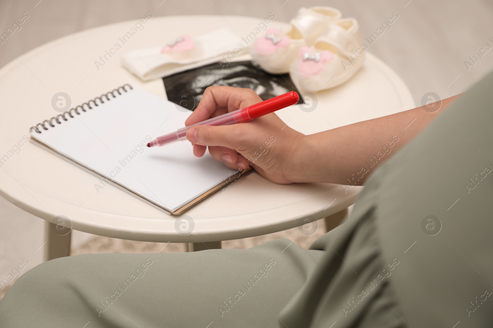 Photo of Pregnant woman writing baby names list at small white table, closeup