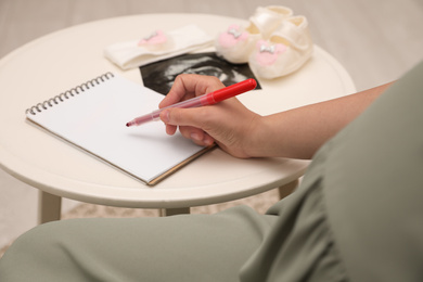 Photo of Pregnant woman writing baby names list at small white table, closeup