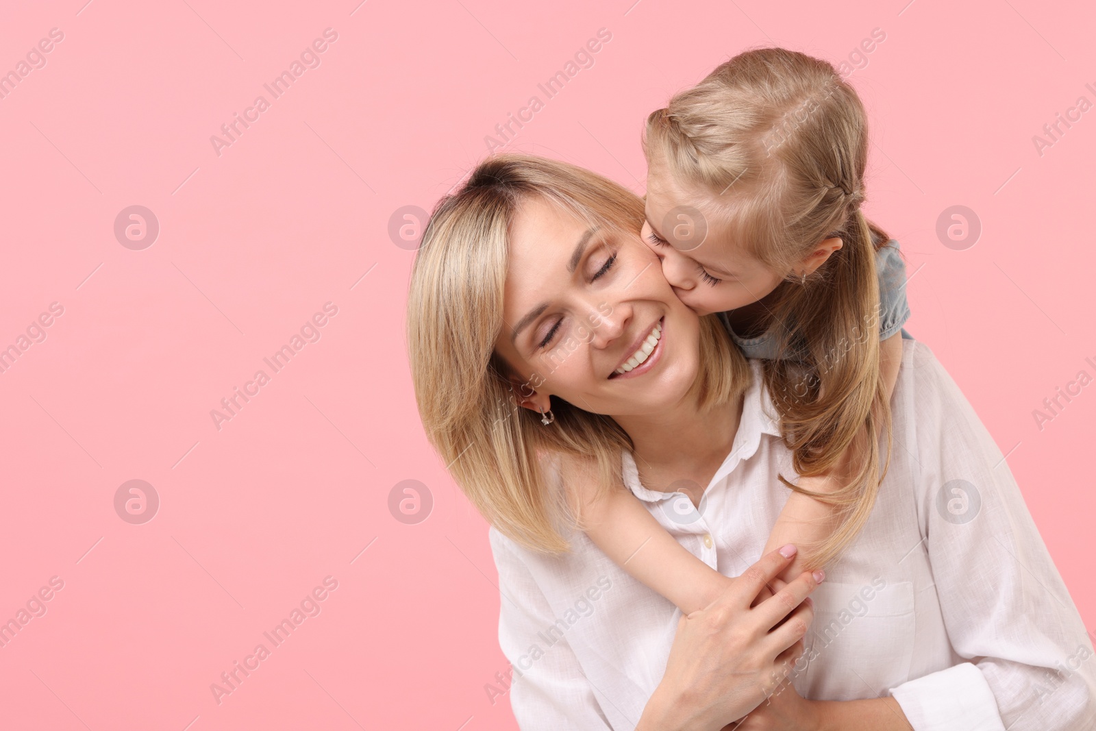 Photo of Daughter hugging and kissing her happy mother on pink background. Space for text