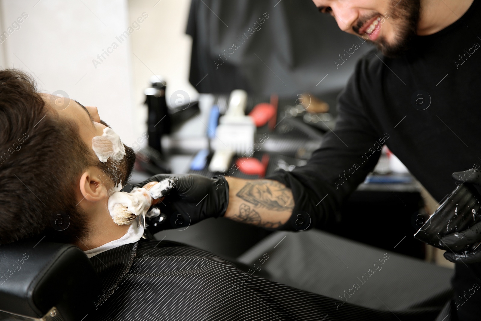 Photo of Professional hairdresser applying shaving foam onto client's skin in barbershop