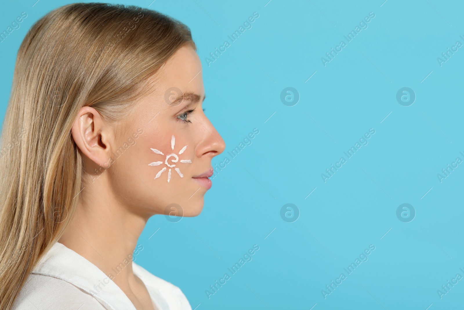 Photo of Beautiful young woman with sun protection cream on her face against light blue background, space for text