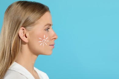 Beautiful young woman with sun protection cream on her face against light blue background, space for text