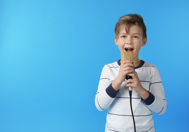 Cute boy singing in microphone on color background. Space for text