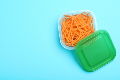 Photo of Fresh shredded carrots in glass container on light blue background, top view. Space for text