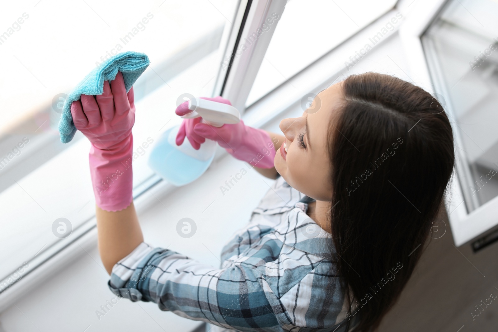 Photo of Young woman cleaning window glass at home